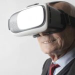 Virtual Reality And Augmented Reality - Smiling elderly gentleman wearing classy suit experiencing virtual reality while using modern headset on white background