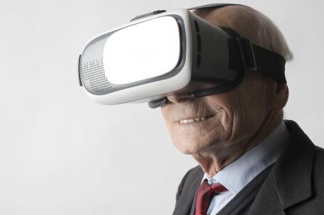 Virtual Reality And Augmented Reality - Smiling elderly gentleman wearing classy suit experiencing virtual reality while using modern headset on white background