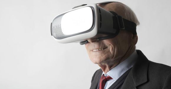 Virtual Reality And Augmented Reality - Smiling elderly gentleman wearing classy suit experiencing virtual reality while using modern headset on white background