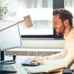 Technology - Man in White Dress Shirt Sitting on Black Rolling Chair While Facing Black Computer Set and Smiling