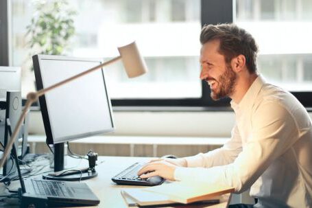 Technology - Man in White Dress Shirt Sitting on Black Rolling Chair While Facing Black Computer Set and Smiling