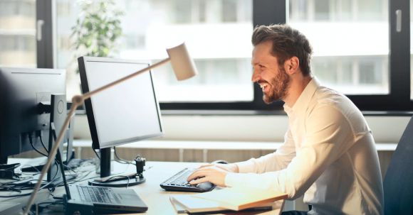 Technology - Man in White Dress Shirt Sitting on Black Rolling Chair While Facing Black Computer Set and Smiling