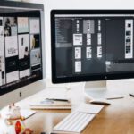 Web Design - Two Imac's With Keyboard and Phones on Desk