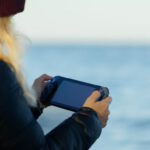 Pc - a woman holding a game controller in front of a body of water